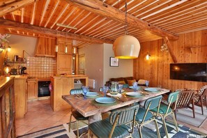 Un interior de madera con una mesa de comedor preparada para seis personas, rodeada de sillas tapizadas en verde.