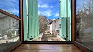 Una habitación con ventanas amplias y suelo de madera, con vistas a una montaña nevada y edificios cercanos.