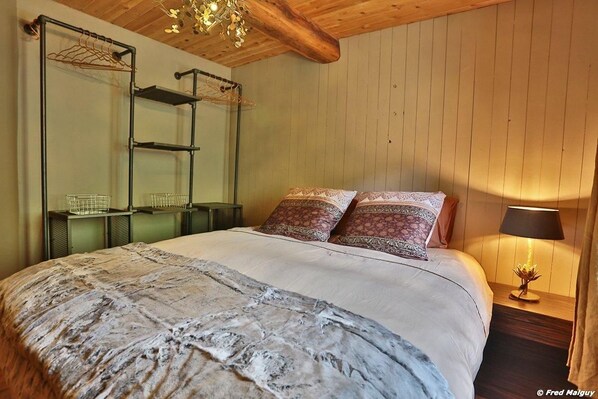 Un dormitorio con cama, lámpara colgante, mesita de noche con lámpara y estante con espejo y cestas de almacenamiento.