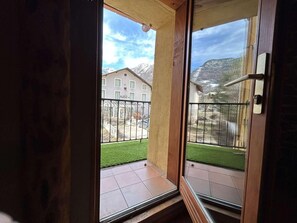 Vista desde un balcón con puerta de cristal, suelo de baldosas y un pequeño espacio cubierto de césped.