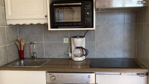 Eine kleine Küche mit weißen Schränken, einer integrierten Mikrowelle, einer Kaffeemaschine und einem Geschirrspüler.