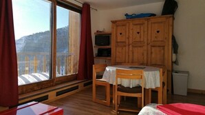 Ein Zimmer mit Holztisch und -stühlen, einem kleinen Schrank, einem Fernseher und einem Fenster mit Blick auf eine verschneite Landschaft.