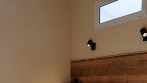 Ein kleines Zimmer mit einem Einzelbett, einem Holzkopfstück, einem kleinen Fenster und zwei Wandleuchten.