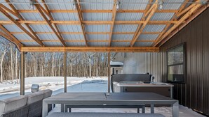 Un espacio al aire libre cubierto con mesa y bancos, un jacuzzi y vistas a un paisaje nevado con árboles.