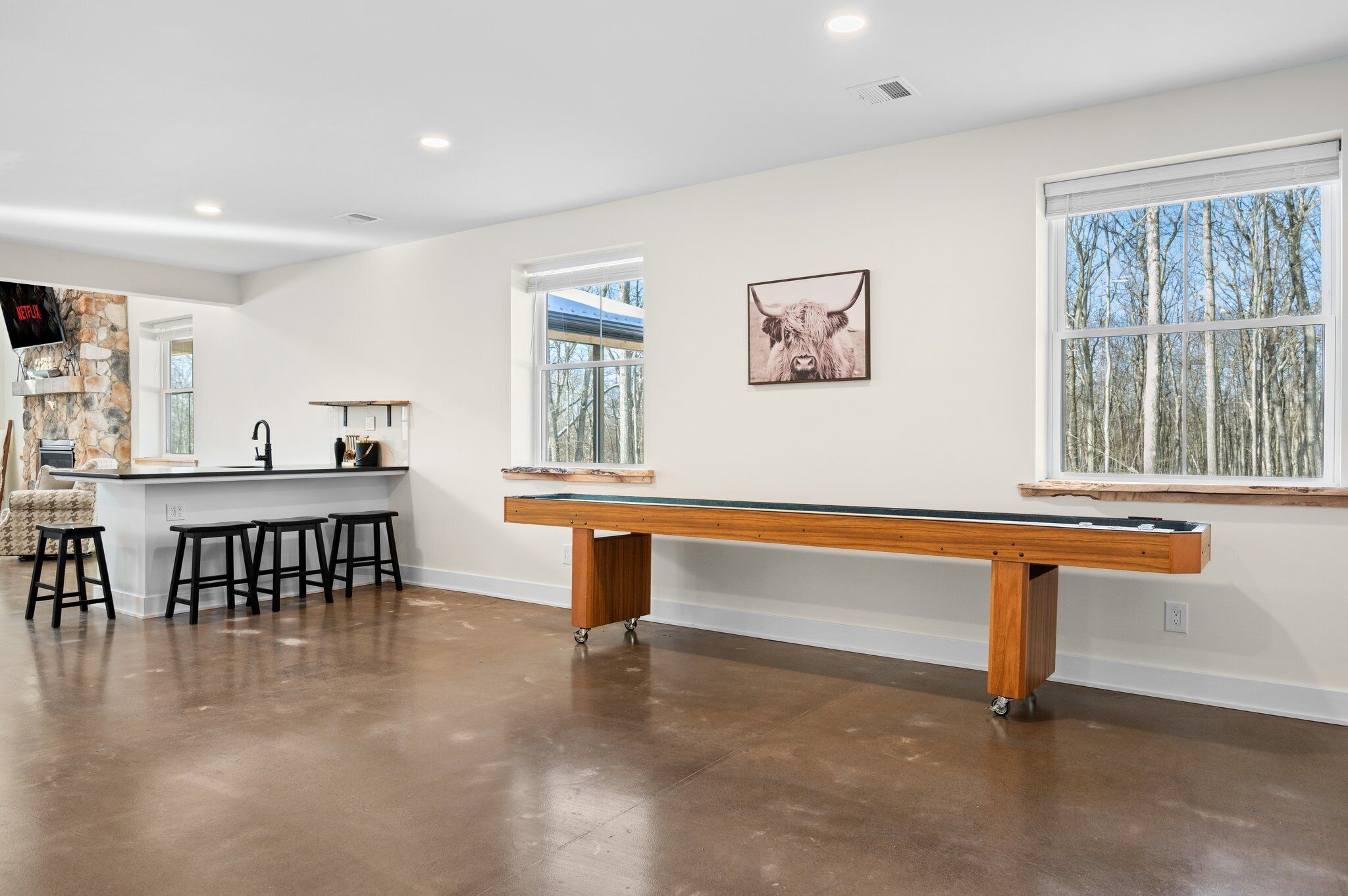 A pool table in a spacious room with a stone accent wall, a bar area, and large windows.