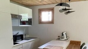 A compact kitchen with white cabinets, a wooden dining table, and a patterned rug. - 2nd floor, balcony, fireplace or stove, parking, tv, ski locker, 40m², Le Grand Bornand (Le Grand-Bornand)