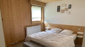 A bedroom with a wooden headboard, a single bed with white bedding, a bedside table, and a small bench. - 2nd floor, balcony, fireplace or stove, parking, tv, ski locker, 40m², Le Grand Bornand (Le Grand-Bornand)