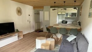 A modern living room with a grey sofa, a flat-screen TV, and a wooden coffee table. There is a small round side table and a kitchen area with a dining table and chairs. - 2nd floor, balcony, fireplace or stove, parking, tv, ski locker, 40m², Le Grand Bornand (Le Grand-Bornand)