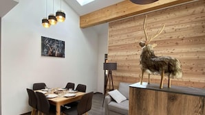 Een moderne eethoek met een houten tafel en stoelen, een plafondlamp en een hertenbeeld op een houten platform.