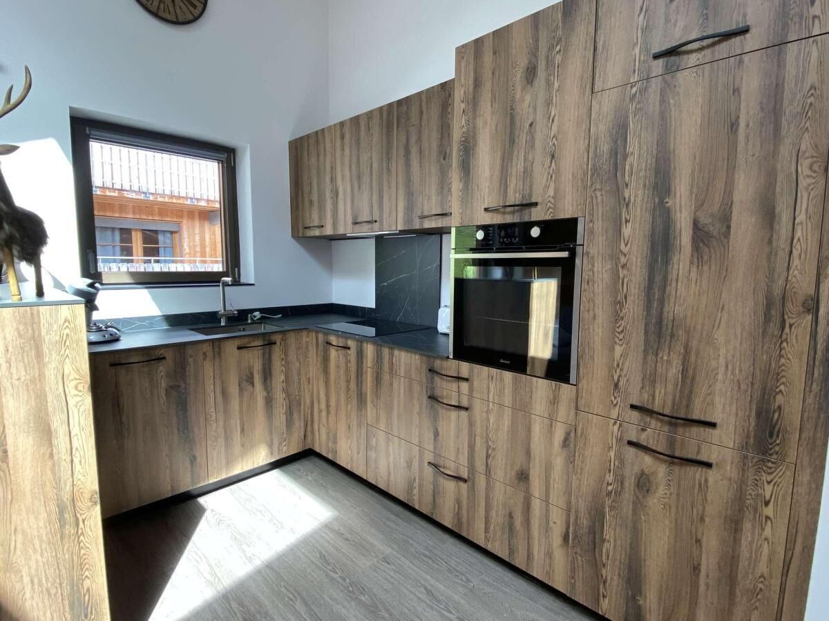 A modern kitchen with wooden cabinets, a built-in oven, and a window providing natural light.