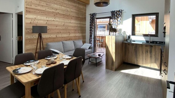 Een moderne keuken met houten kasten, een eetgedeelte met een tafel voor vier personen, en een gezellige zithoek met een bank.