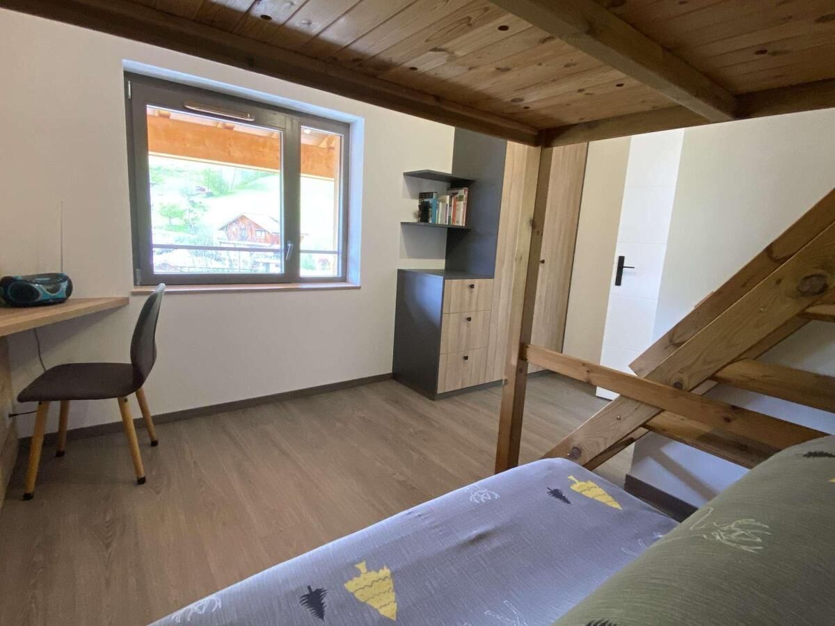 Et soveværelse med køjeseng, skrivebord, stol og et vindue med udsigt til et hus.