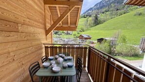 Een houten terras met een eettafel, met uitzicht op een groen landschap.