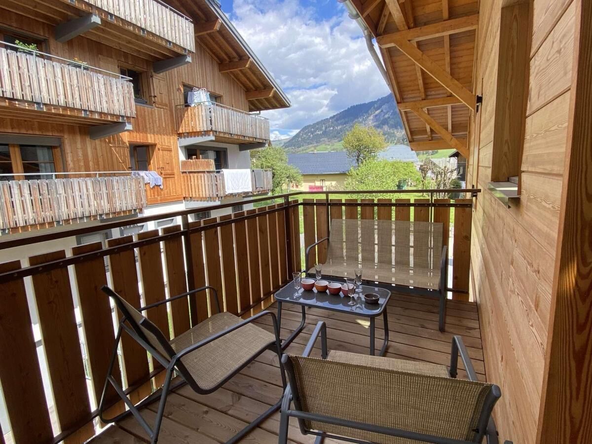 A wooden balcony with a table and chairs, overlooking a mountainous landscape.