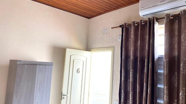 A room with a wooden ceiling, a white door with the number 6, a grey wardrobe, and brown patterned curtains. - Two suites just 100 meters from the central square and 20 km from Pedra do Baú. (São Bento do Sapucaí)