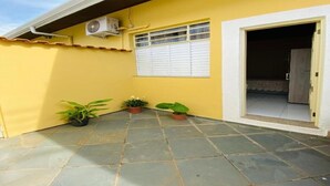 A yellow building with a tiled patio, a window with white shutters, and a door leading to an interior space. - Two suites just 100 meters from the central square and 20 km from Pedra do Baú. (São Bento do Sapucaí)