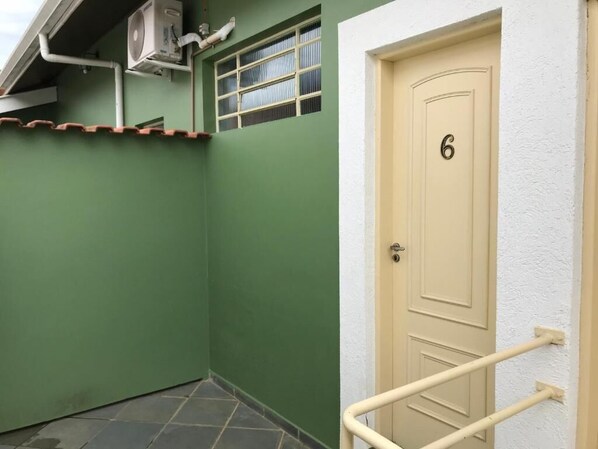 A green exterior wall with a beige door marked with the number 6, a small window, and a white railing.