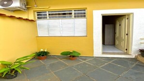 A yellow house with a tiled patio, a window with shutters, and a door marked with the number 6. - Two suites just 100 meters from the central square and 20 km from Pedra do Baú. (São Bento do Sapucaí)