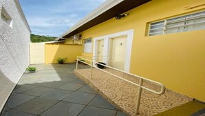 A yellow building with a tiled patio, a metal handrail, and a door marked with the number 5. - Two suites just 100 meters from the central square and 20 km from Pedra do Baú. (São Bento do Sapucaí)