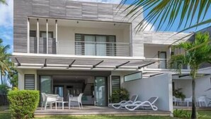 A modern two-story house with a flat roof, large windows, and a covered patio area with outdoor furniture. - Unique Villa Feet in the water-pool- Grand Baie (Grand Baie)