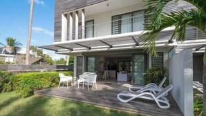 A modern two-story house with a covered patio area, outdoor seating, and lush greenery. - Unique Villa Feet in the water-pool- Grand Baie (Grand Baie)