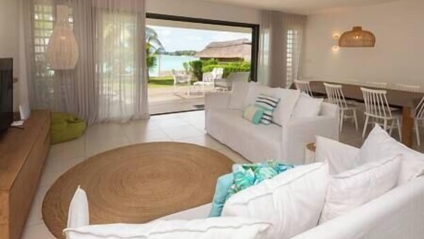 A modern living room with a white sofa, a round wooden rug, and a dining area with white chairs. - Unique Villa Feet in the water-pool- Grand Baie (Grand Baie)