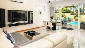 A modern living room with a flat-screen TV, a dining area, and a poolside view. - To complete (Cap Malheureux)