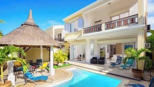 A two-story hotel with a swimming pool, outdoor seating, and a thatched-roof structure. - To complete (Cap Malheureux)