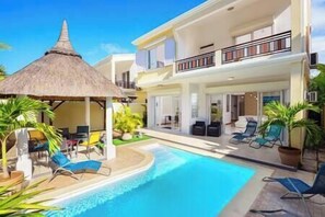 Un hôtel de deux étages doté d’une piscine, d’un espace extérieur aménagé et d’une structure surmontée d’un toit de chaume.