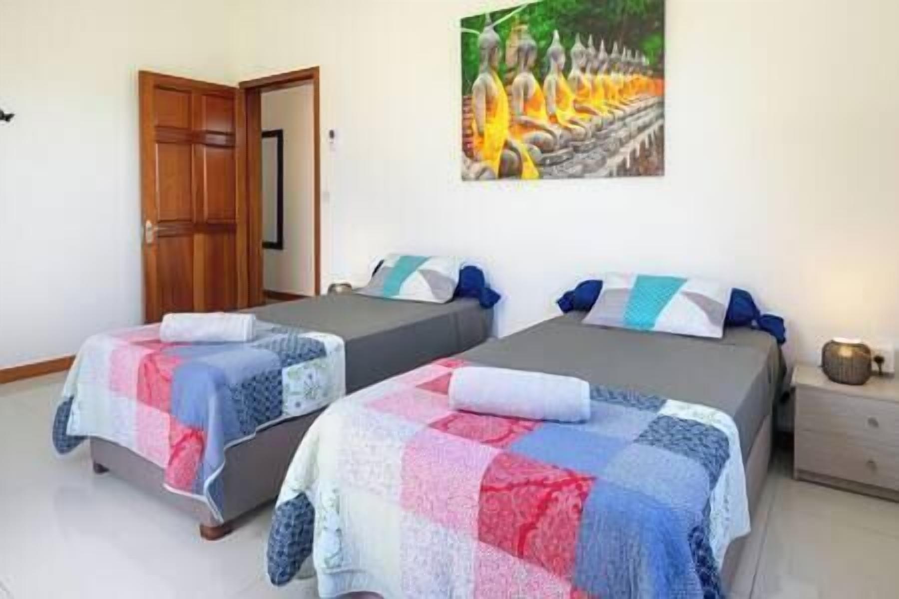 Una habitación con dos camas, cada una con una manta acolchada y almohadas. Hay una puerta de madera y un cuadro en la pared.