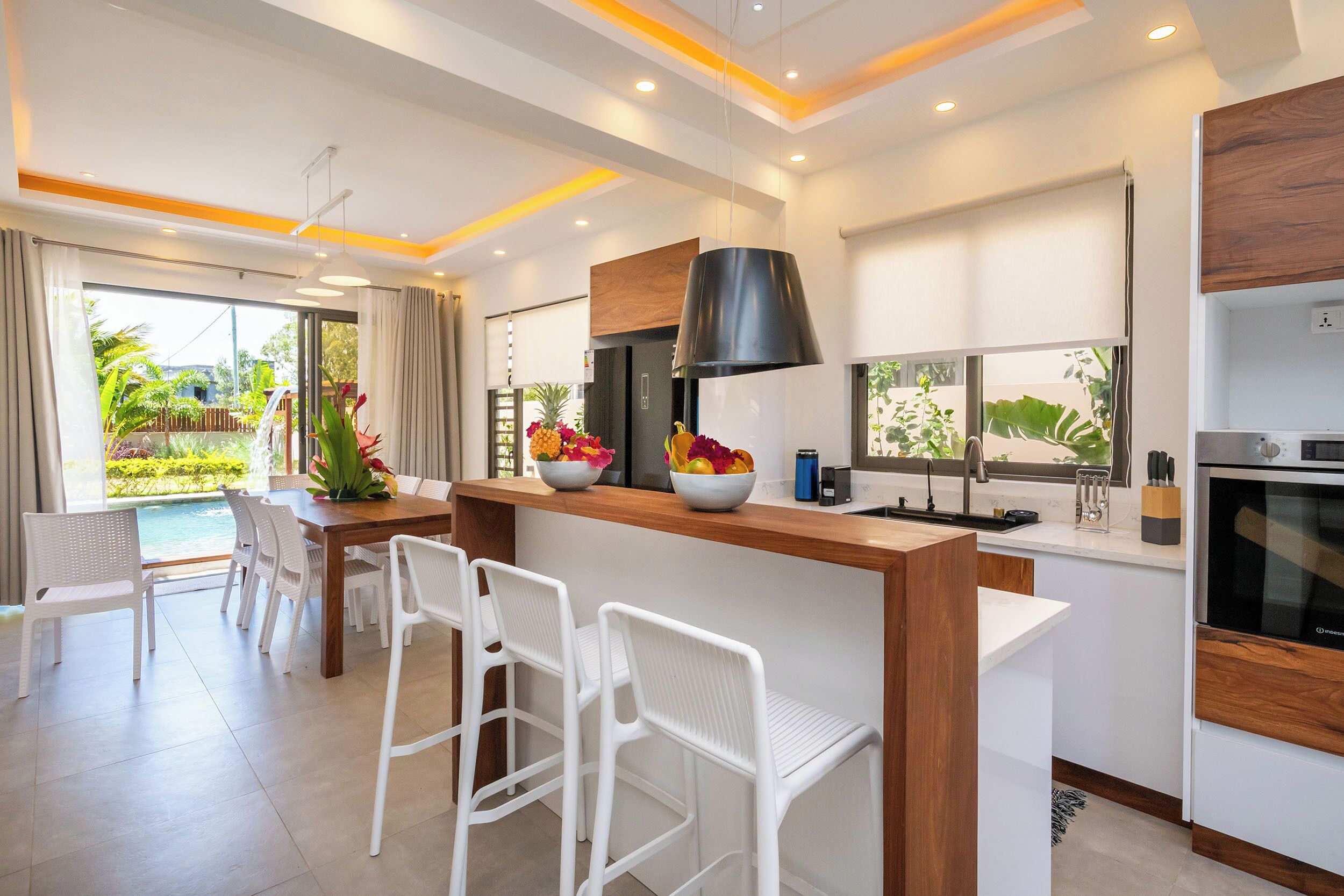 Une cuisine moderne dotée d’un îlot central, de tabourets de bar et d’un coin repas offrant une vue sur l’extérieur.