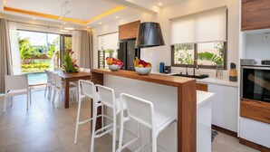 Une cuisine moderne dotée d’un îlot central, de tabourets de bar et d’un coin repas offrant une vue sur l’extérieur.
