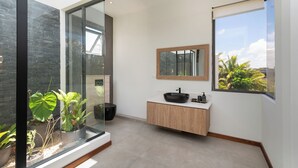 Une salle de bain moderne avec une grande fenêtre, un meuble-lavabo en bois, un lavabo noir et un miroir.