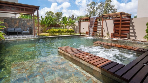 Une piscine aux eaux cristallines, agrémentée d’une terrasse en bois et d’une cascade.