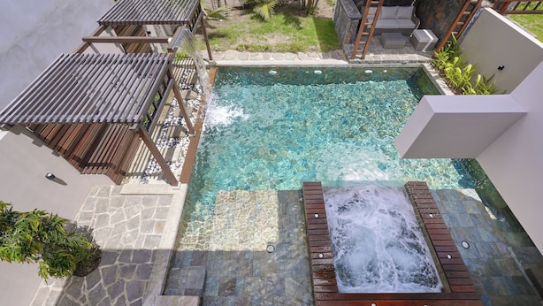 Una piscina cristalina con jacuzzi, terraza de madera, escalones de piedra y una pequeña zona ajardinada.