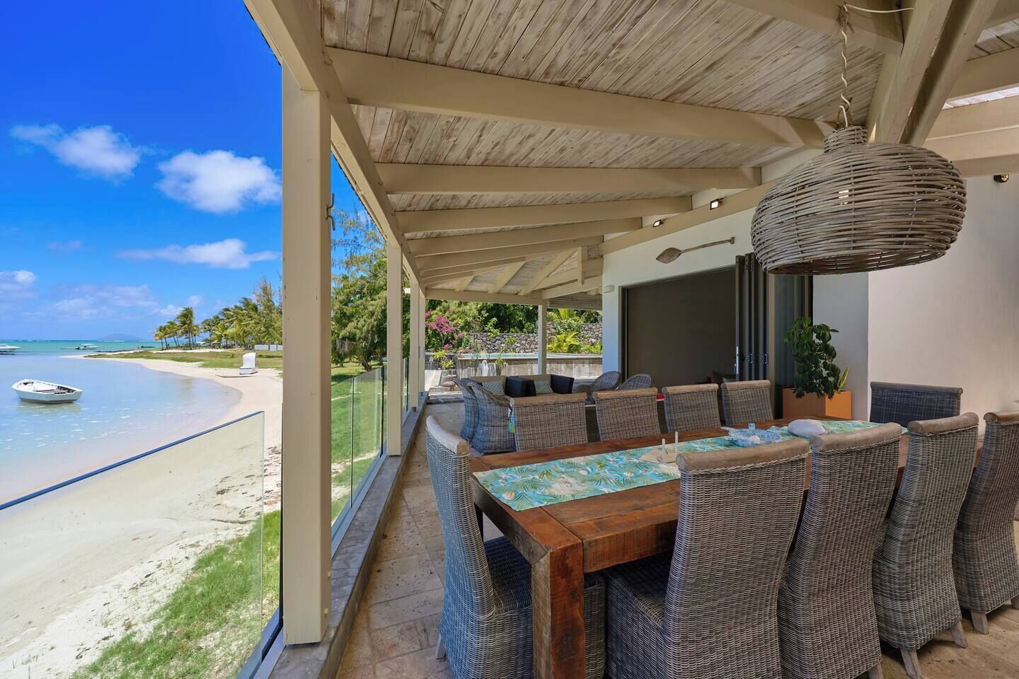 A covered outdoor dining area with wicker furniture, a wooden table, and a hanging light fixture.
