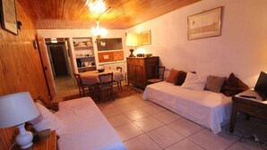 A cozy room with two beds, a wooden ceiling, a dining area with a table and chairs, and a cabinet.