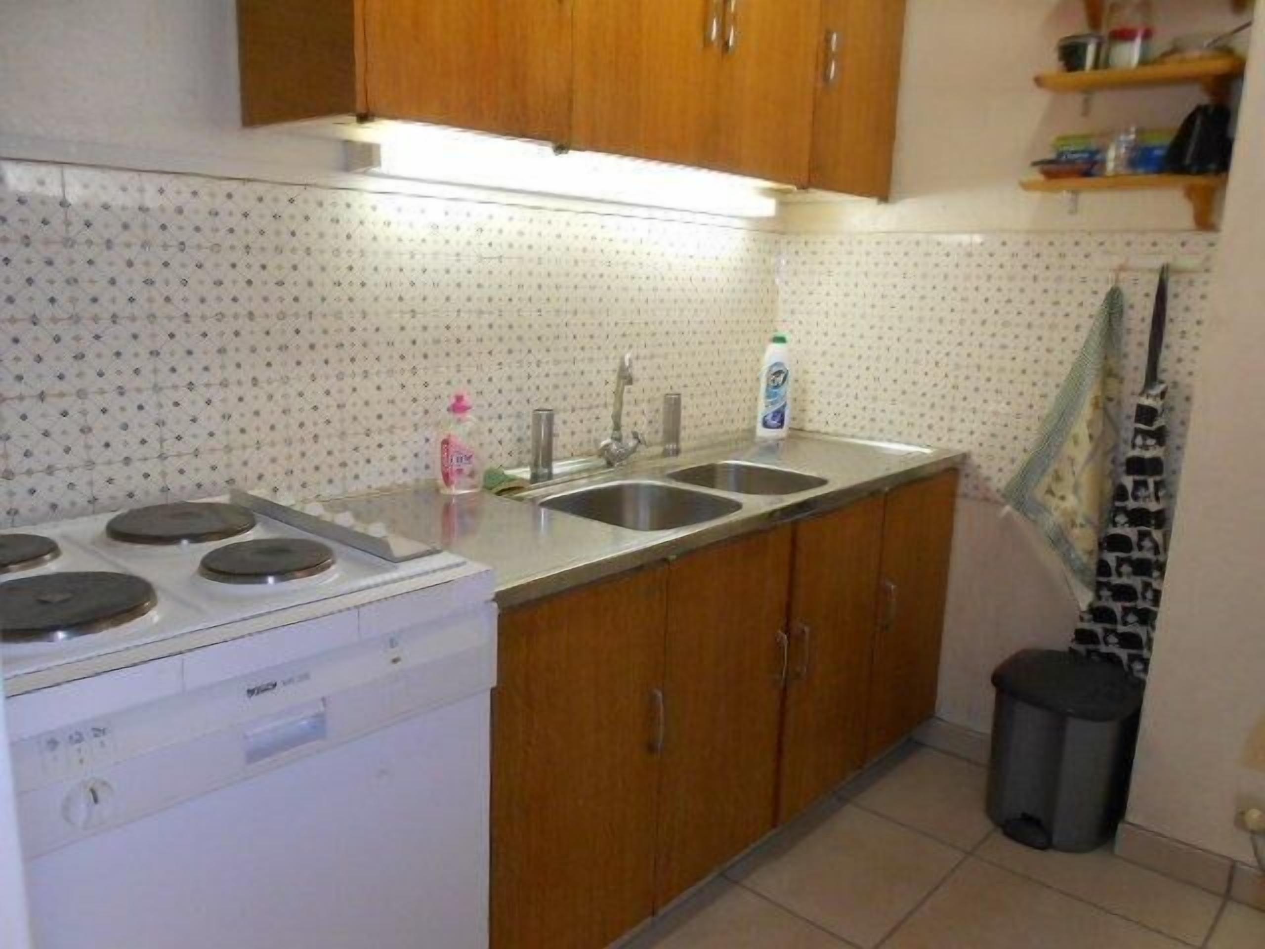 A kitchen with a stove, two sinks, wooden cabinets, and a tiled backsplash.