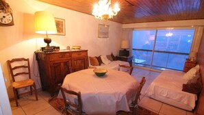 A cozy room with a round dining table, a bed with white bedding, a wooden dresser, and a large window offering a view.