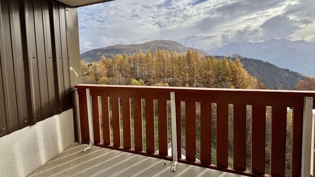Un balcon avec vue sur les arbres aux couleurs automnales et les montagnes.