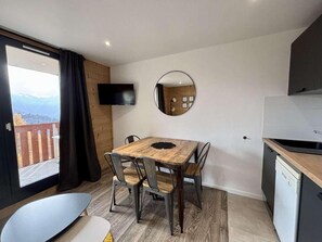 A modern kitchen with a built-in dishwasher, a dining area with a wooden table and metal chairs, and a large window offering a view of a mountainous landscape. - 130m from ski slopes, 6th floor, view open, swimming pool, sauna, balcony, tv, ski locker, 30m² (L'Alpe d'Huez)
