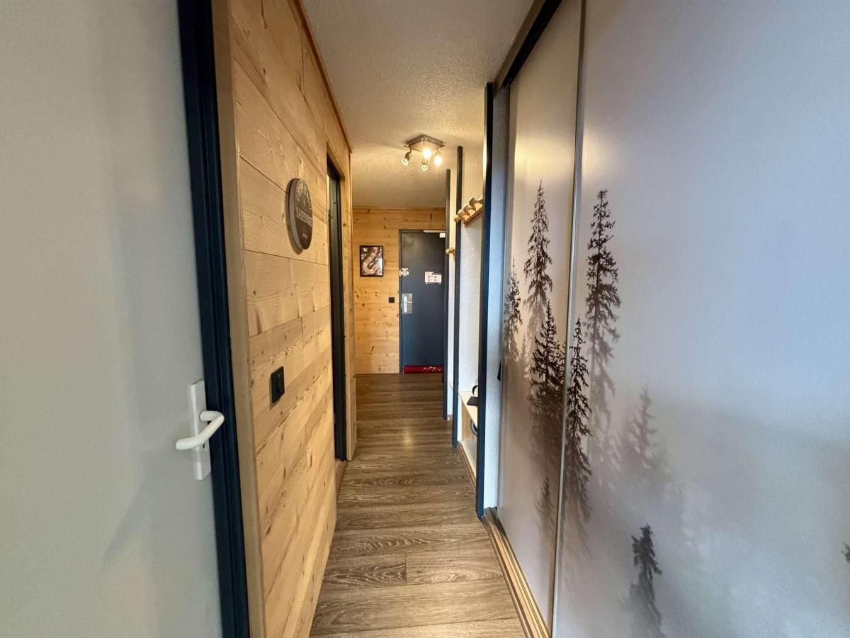 Een gang met houten wanden en een houten vloer, die leidt naar een kamer met een deur en een klok aan de muur.