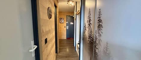 A hallway with wooden walls and a wooden floor, leading to a room with a door and a wall-mounted clock.