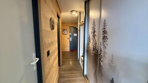 Un couloir aux murs et au sol en bois, qui mène à une pièce dotée d’une porte et d’une horloge fixée au mur.