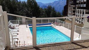 Une piscine avec vue sur les montagnes, entourée de rampes blanches et de chaises longues.