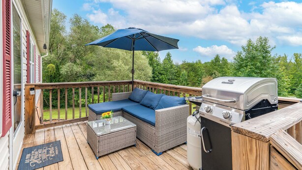 A covered deck with a grill, outdoor furniture, and a view of the surrounding greenery.