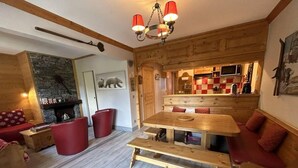 Una sala de estar acogedora con una mesa de madera, sillones tapizados en rojo y una chimenea.