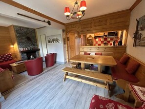 A cozy living room with a wooden table, red upholstered chairs, and a fireplace.