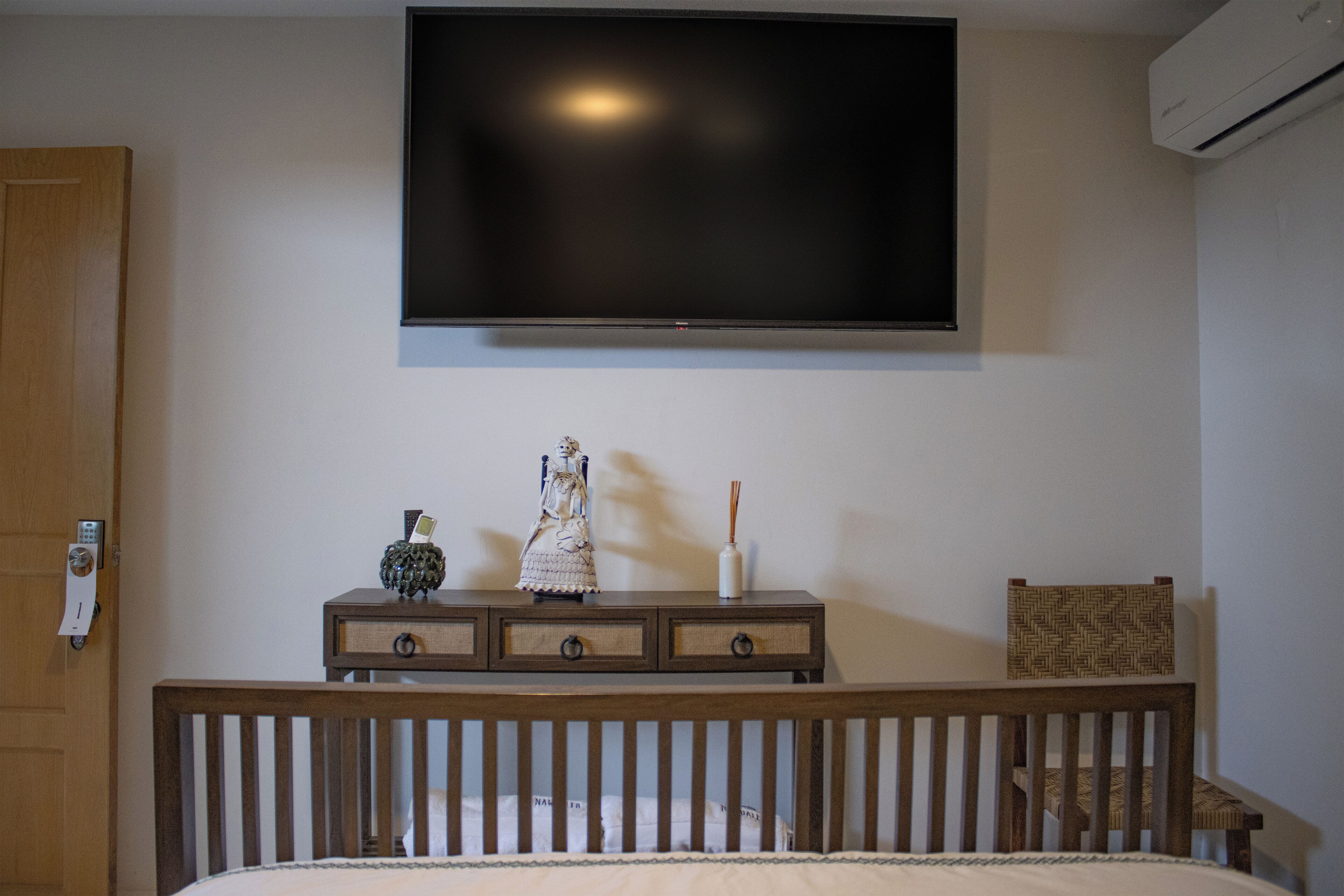 Un dormitorio con cama, cómoda, televisor montado en la pared y una puerta con cerradura.