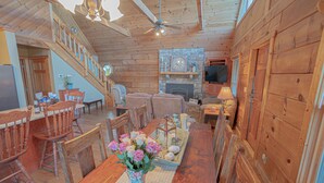 L’intérieur d’un chalet en bois comprend un coin repas, une cheminée et un ventilateur de plafond.